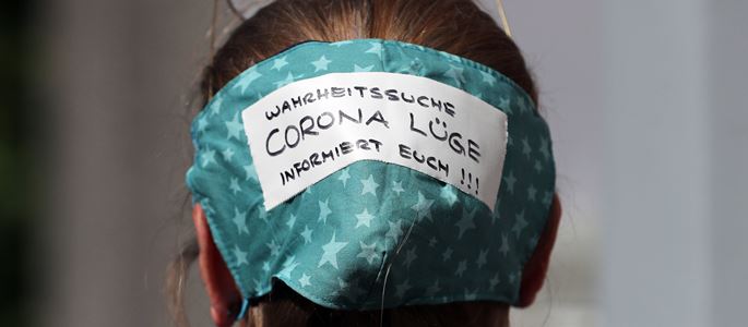 Eine Frau hat ihre Atemschutzmaske auf dem Hinterkopf mit der Aufschrift Corona Lüge