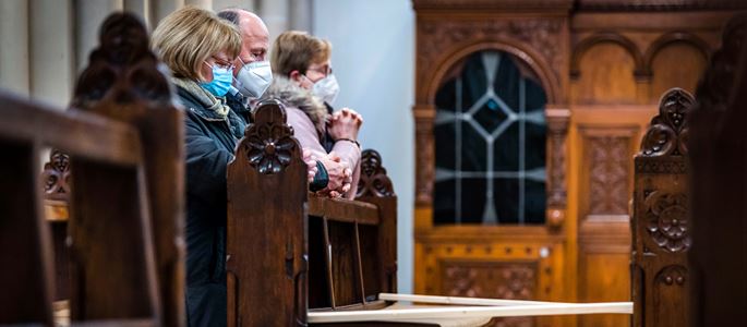 Gottesdienstbesucher tragen Mundschutz und Knien in einer Kirche
